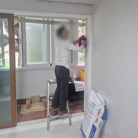 사다리 위에서 베란다 쪽 창문 안쪽을 닦는 작업 모습