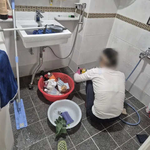 세정 용품과 대야를 두고 욕실 바닥 모서리를 닦는 작업 모습