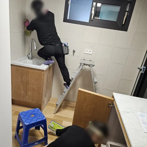 싱크대 하부장 안쪽과 위쪽 벽면을 두 사람이 나누어 닦는 작업 모습