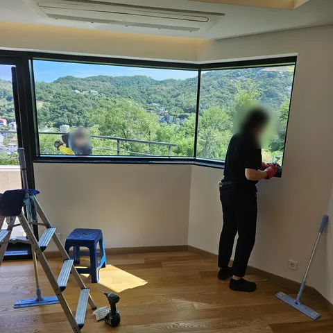 코너 창을 닦는 작업자와 사다리, 밀대가 보이는 방