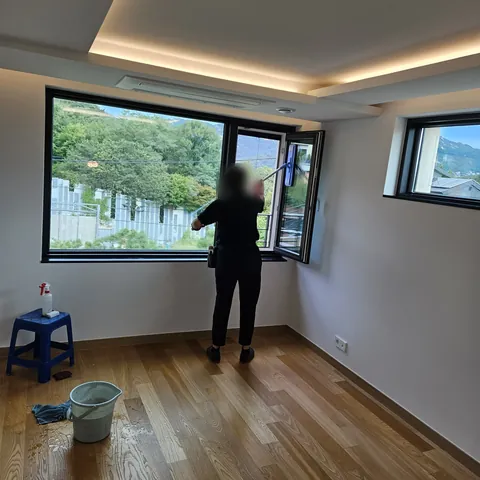 창문을 닦는 작업자와 양동이가 놓인 원목 마루 방