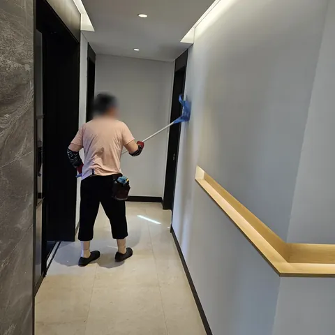 복도 벽 상단을 밀대로 닦는 작업 모습